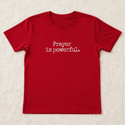 Red t-shirt flat lay on beige linen background with small centered white distressed typewriter text Prayer is powerful dot exact font match